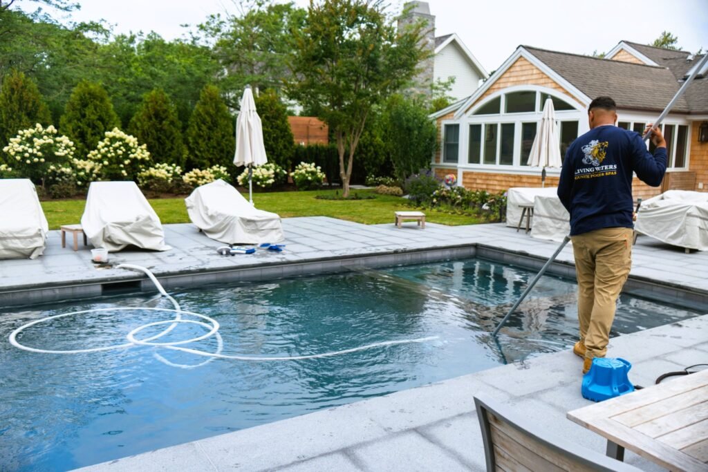 Pool technician performing routine maintenance and water care at an outdoor residential swimming pool on Cape Cod