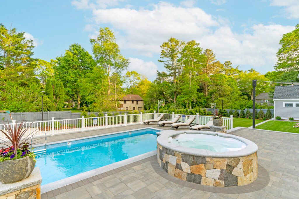 Outdoor hot tub next to a residential swimming pool with stone surround at a Cape Cod property