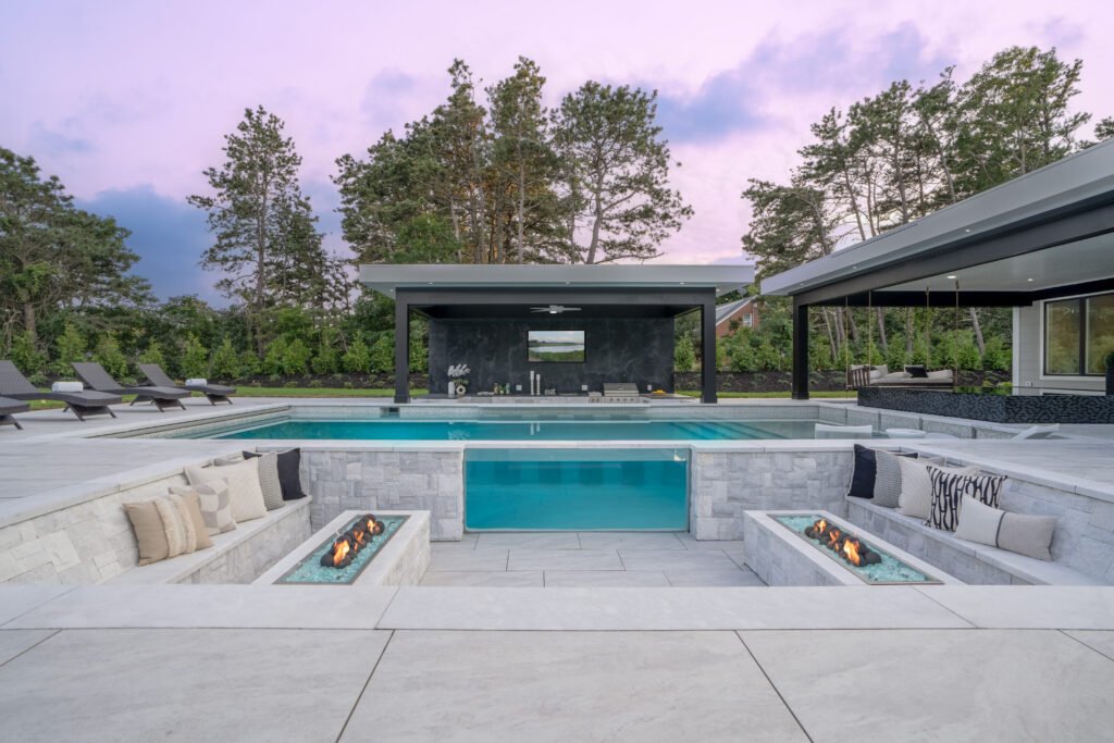 Sunken outdoor fire pit overlooking a residential swimming pool with modern stone design at a Cape Cod property