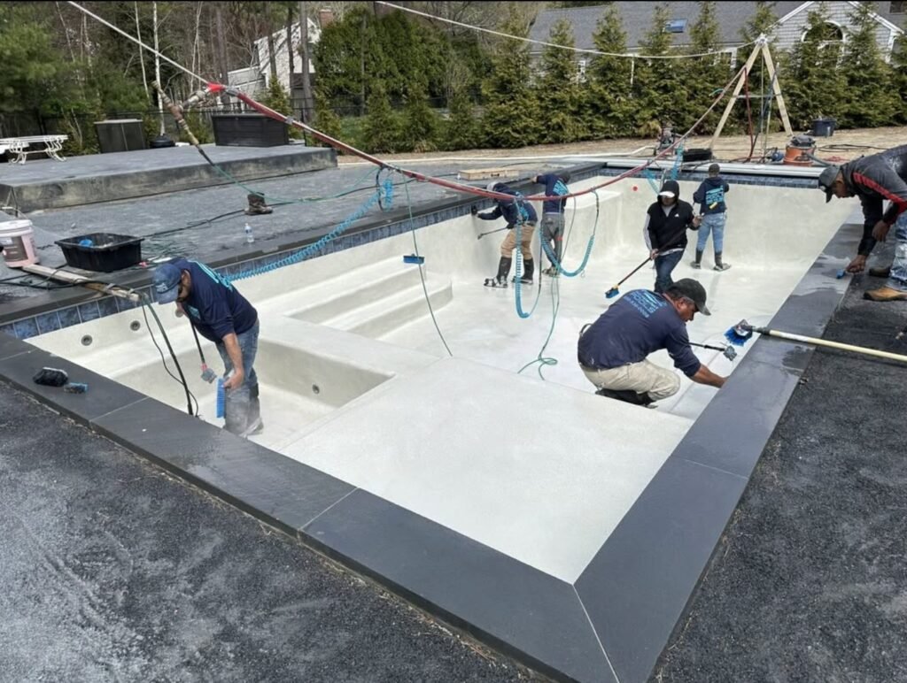 Swimming pool construction work with technicians applying interior finish at a residential outdoor pool on Cape Cod